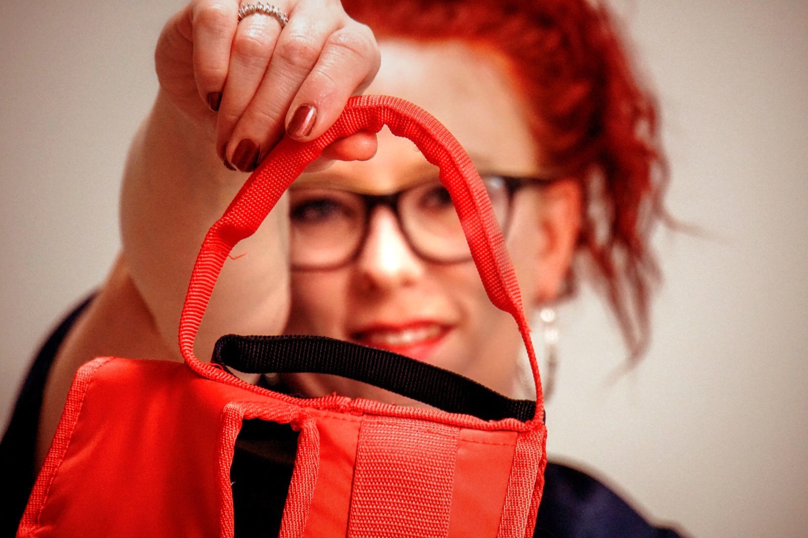 Kuvassa on Satu Lejman. Satulla on silmälasit ja punaiset hiukset. Satu ojentaa kuvassa kameraa kohti punaisen esineen, jossa on sanka.
