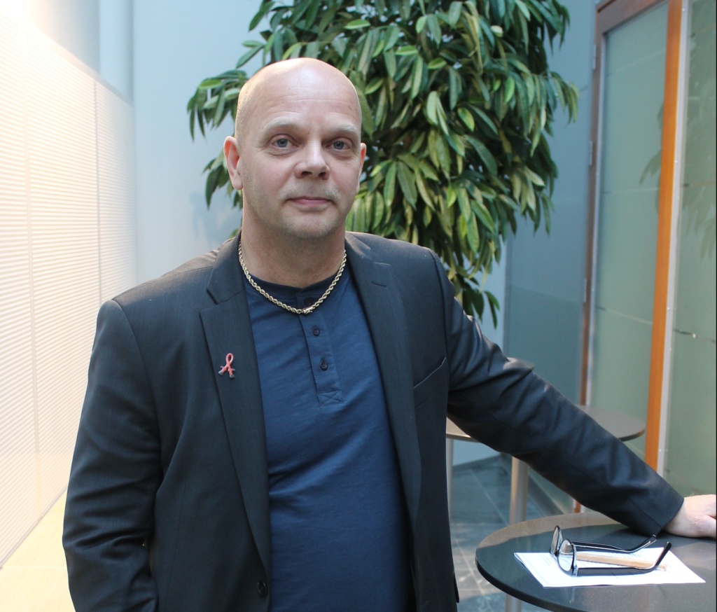 Kuvassa on Ilkka Mustonen. Ilkalla on yllään sininen paita ja puvuntakki. Kuva on otettu toimistoympäristössä.